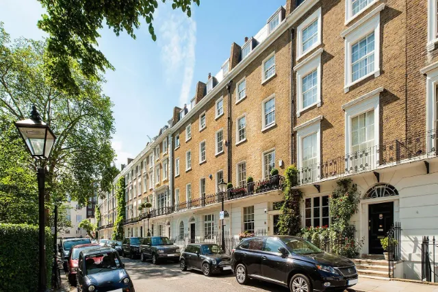 Quiet London residential street with classic brick terraced houses and parked cars, representing pre-booked private transport pickups across the city.